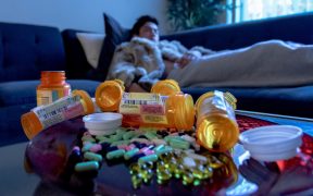 Pills on the table with a person on the couch in the background
