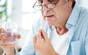 an older white man with glasses taking a pill