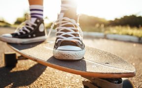 a picture of a skateboard on a road, with two feet in sneakers on it