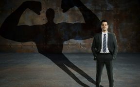 an image of a man in a business suit in front of a wall, and his shadow is in the strong man shape