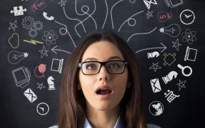 a Caucasian woman with brown hair and glasses with her mouth open in surprise in front of a blackboard. On the blackboard, a bunch of images drawn that are icons for various internet and computer things.