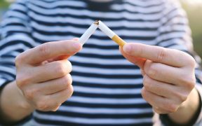 a cropped photo of a person in a blue and white stripped shirt, breaking a cigarette in their hands