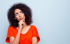 an African American woman in an orange shirt, looking thoughtful, in front of a light blue background