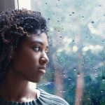 a Black woman looking out the window as it rains