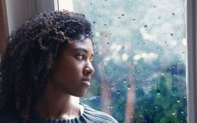 a Black woman looking out the window as it rains
