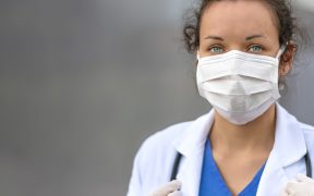 an image of a white woman in doctor's garb with a mask over her face