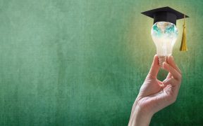 a photo of a hand holding a lit lightbulb with the Earth inside it, and a graduation cap on top of it