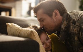 an image of an adult Caucasian man in military fatigues kissing a young girl on the forehead on a couch