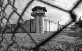 a black and white photo of a prison, behind a chain link fence