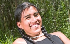 a photo of a young adult American Indian, sitting back in the grass