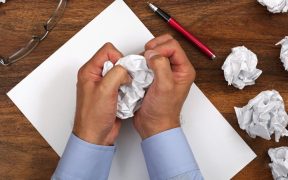 a photo of two male Caucasian hands crumbling up a piece of paper, with several other wads next to it