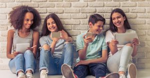 a photo of four teenagers, all sitting with their backs to a brick wall, in casual clothes and talking