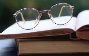 a photo of an open book on top of a closed book on a table, with a pair of glasses on top