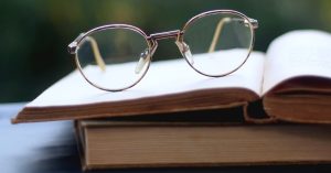 a photo of an open book on top of a closed book on a table, with a pair of glasses on top