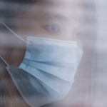a photo of a woman of Asian descent wearing a mask and looking out a window