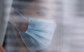a photo of a woman of Asian descent wearing a mask and looking out a window