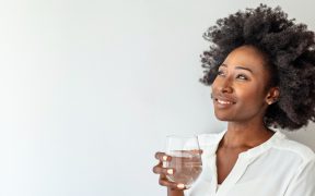 a photo of a Black woman with a drink in her hand, smiling off to the left
