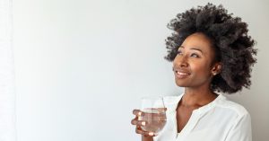 a photo of a Black woman with a drink in her hand, smiling off to the left