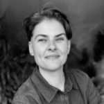 a black and white photo of a white nonbinary person with short dark hair wearing a polo shirt