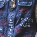 a person in a sleeveless jean jacket with names all over it, with tattoos on the arms