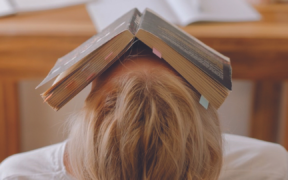 a person with blond hair and white tshirt laying down with a book on their face