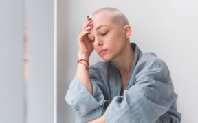 a person in a light blue robe sits on the floor, one hand on their head