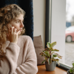 a woman in a pink sweater is looking out the window, looking pensive