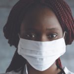 an African American woman in a doctor's jacket wearing a surgical mask