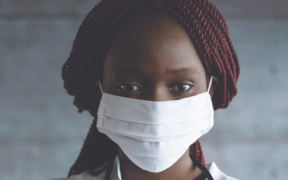 an African American woman in a doctor's jacket wearing a surgical mask