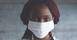 an African American woman in a doctor's jacket wearing a surgical mask