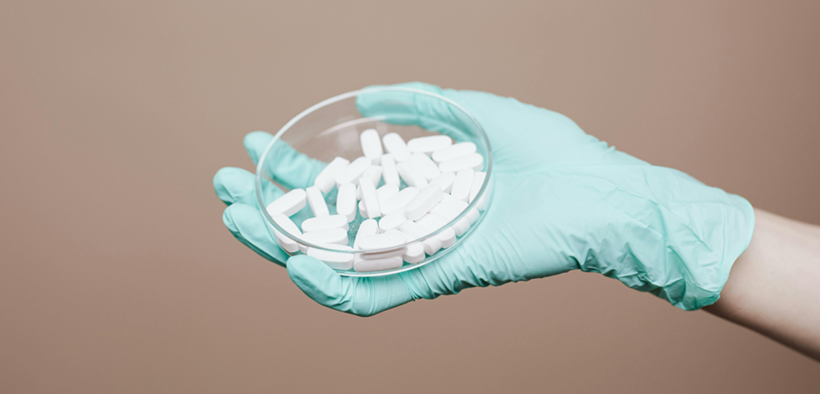 a hand in a medical glove holding a dish full of white pills