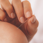 a closeup of a white left shoulder, bare, with a white hand with a needle ready to stick in it