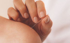 a closeup of a white left shoulder, bare, with a white hand with a needle ready to stick in it