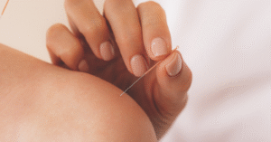 a closeup of a white left shoulder, bare, with a white hand with a needle ready to stick in it