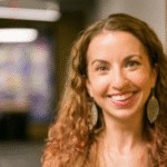 a young white woman with long brown hair, wearing dangling earrings