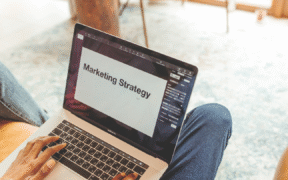 a white person of indistinguishable gender has a laptop open on their lap (wearing jeans0. The laptop says 'marketing strategy'