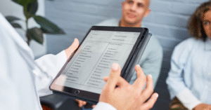 Photo of a tablet in foreground being used to check in patients seated in image background.