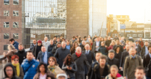Photo of lots of people crossing bridge with faces blurred out. Bright reflection on buildings in background.