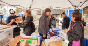 eight people at event distributing Narcan and other supplies, brown paper bags and tubs of supplies in foreground and people in coats interacting under a gray tent